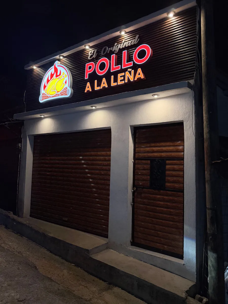 Fachada de El Original Pollo a la Leña de noche, con el rótulo iluminado